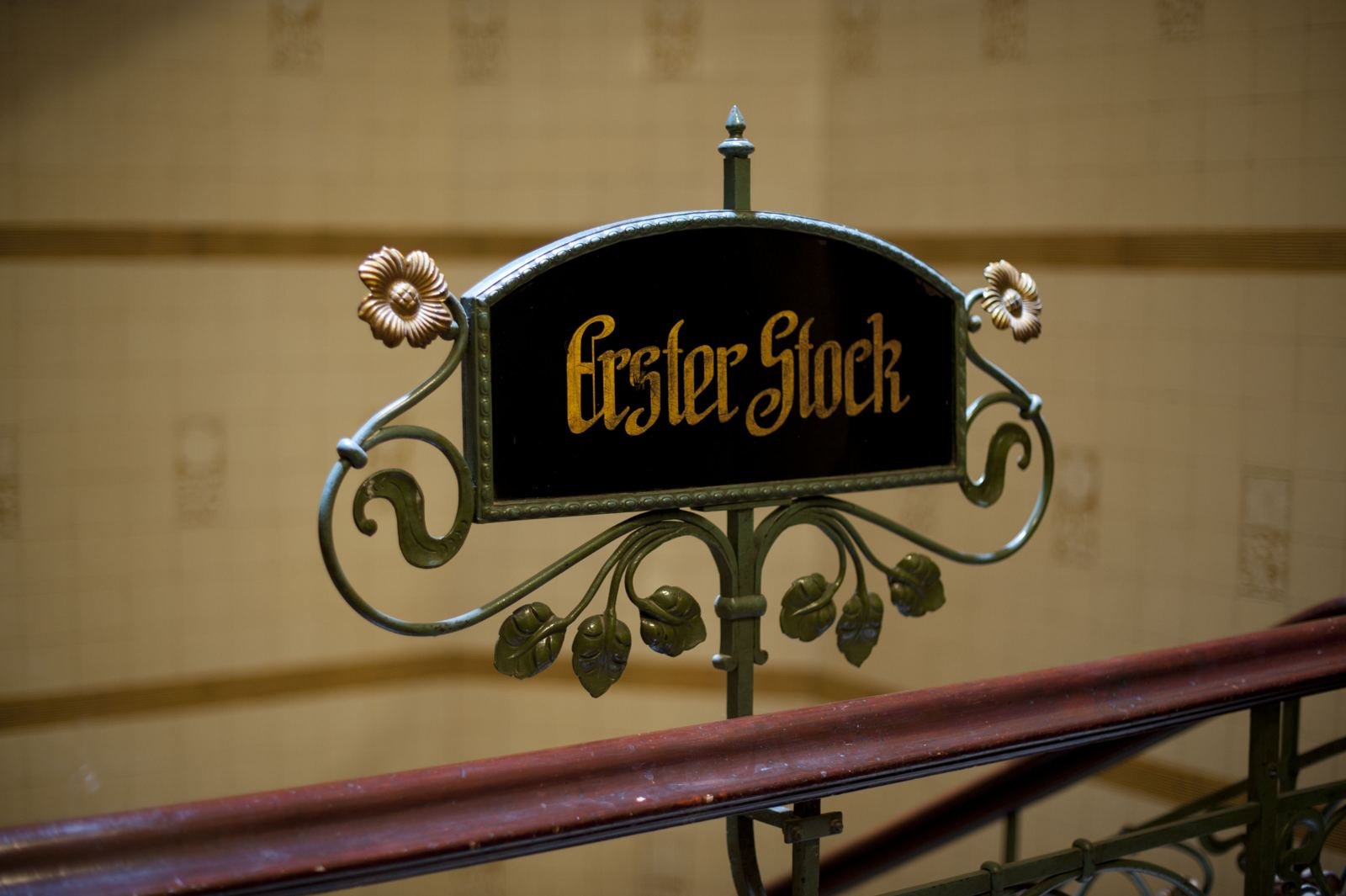 Historisches Etagenschild „Erster Stock“ mit goldener Schrift und schmiedeeisernen Blüten